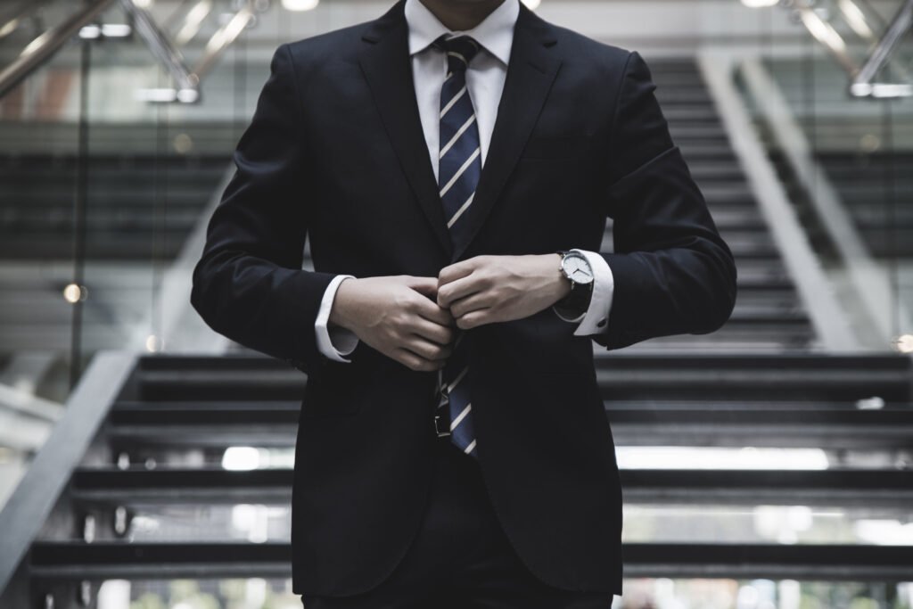 Person in a suit and tie fastening a jacket button